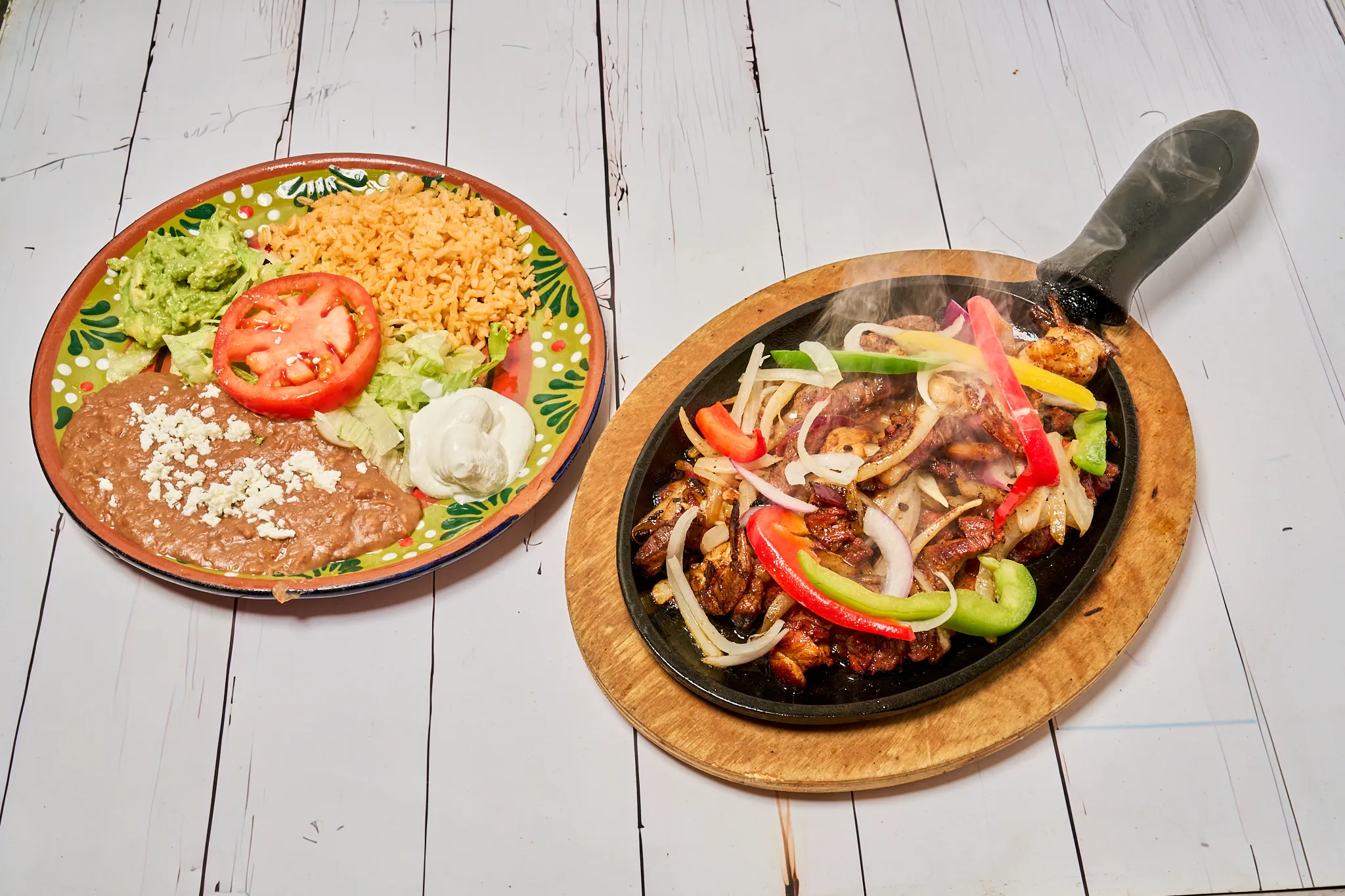 A sizzling fajita platter with rice, beans, and fresh vegetables